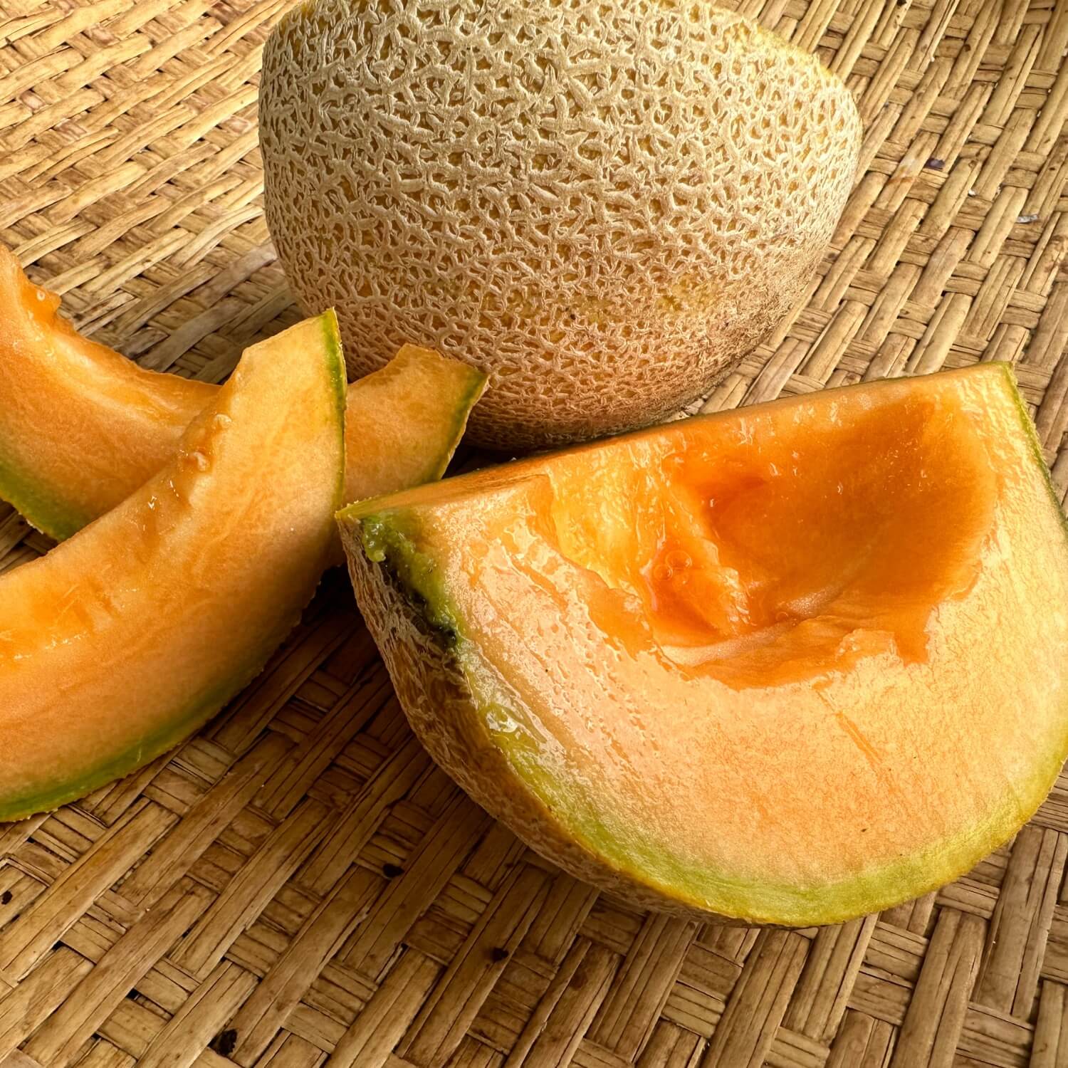 Whole and sliced Mountain Honey Melon on a woven surface