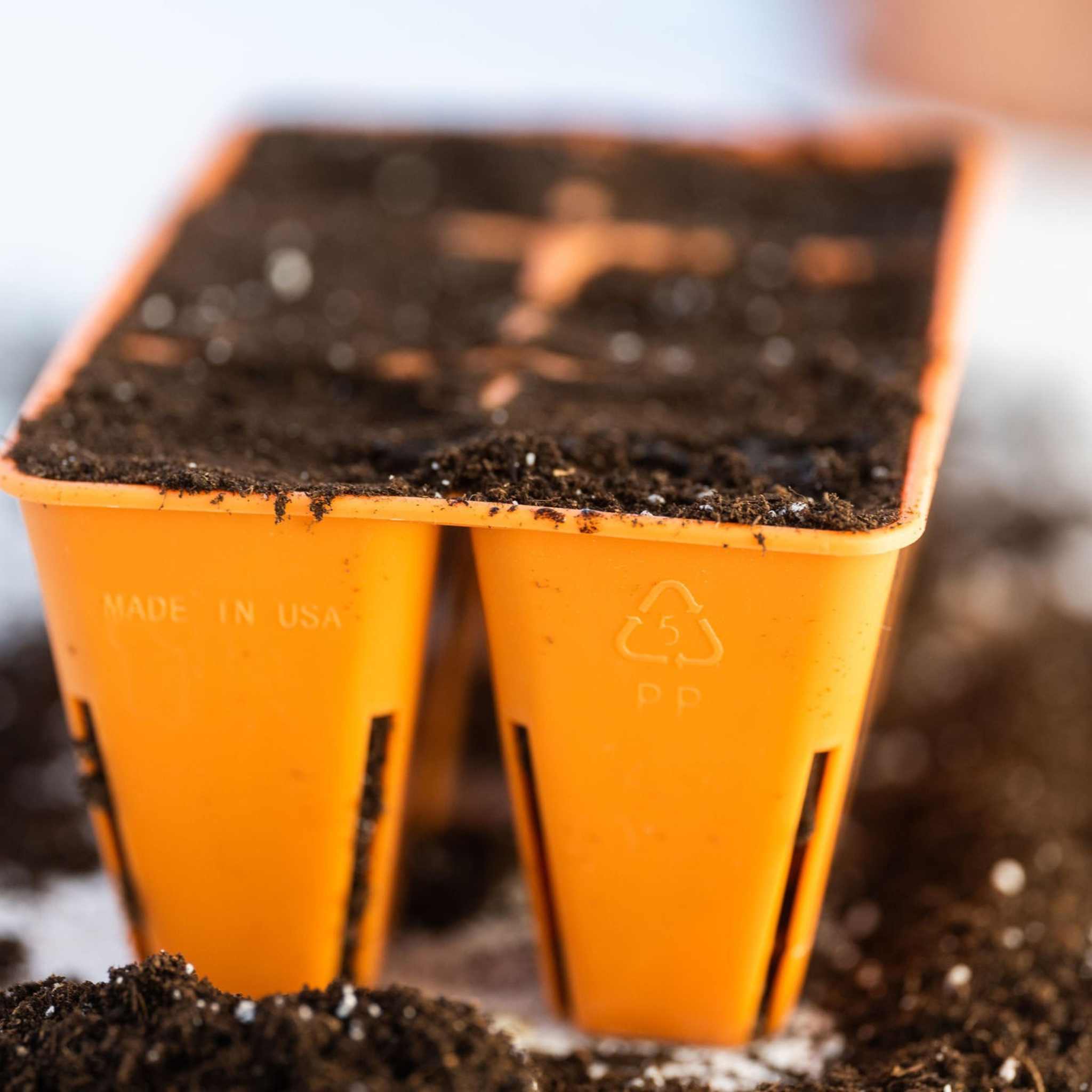 Two orange plastic pots with soil on a blurred background 