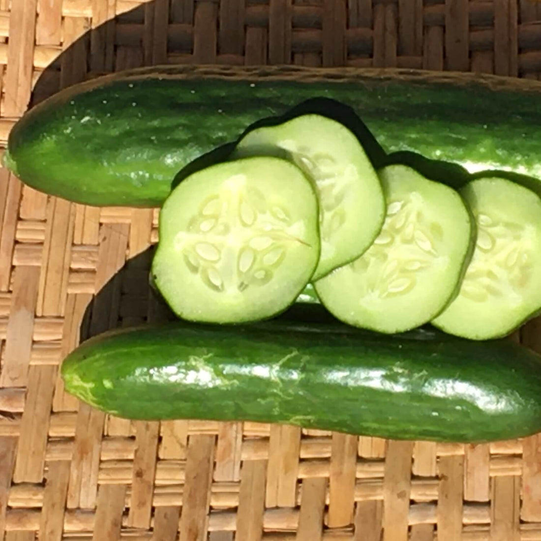 Whole and sliced Persian cucumbers on a woven surface