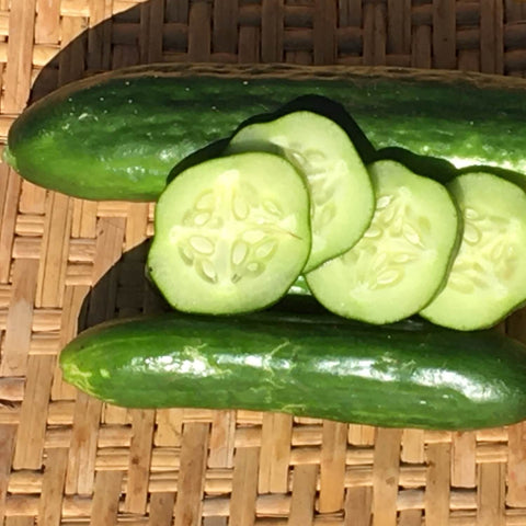 Whole and sliced Persian cucumbers on a woven surface