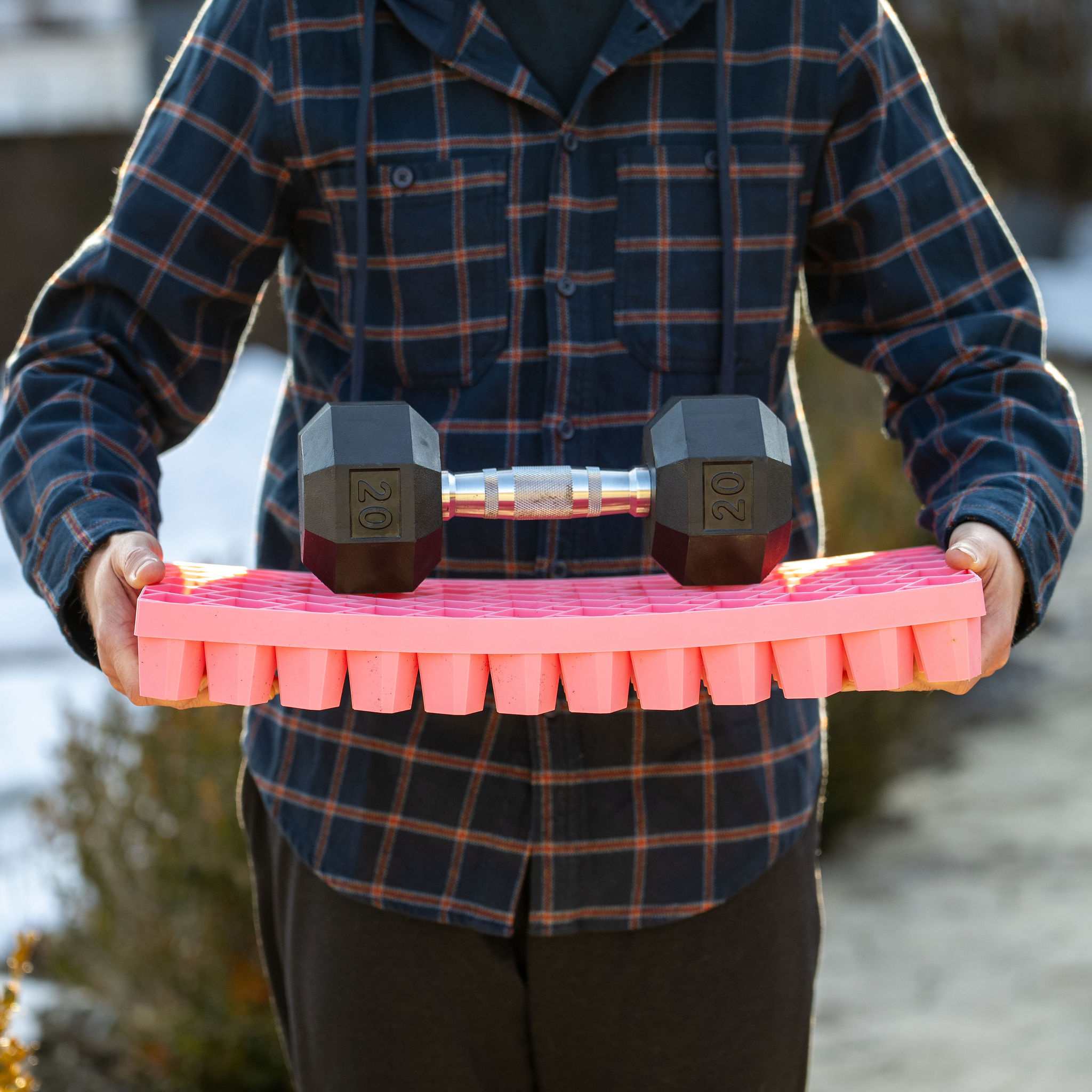 Person holding a pink propagation tray with a 20 lb. dumbbell on top, outdoors. 