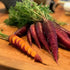 A bunch of purple-skinned carrots with an orange core, freshly harvested and placed on a wooden cutting board.